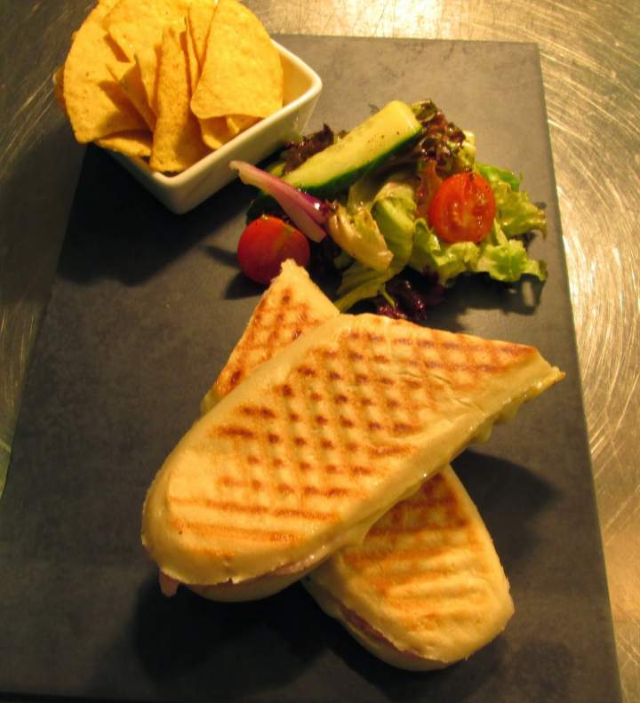Baguette with cheese and ham served with nacho chips and salad